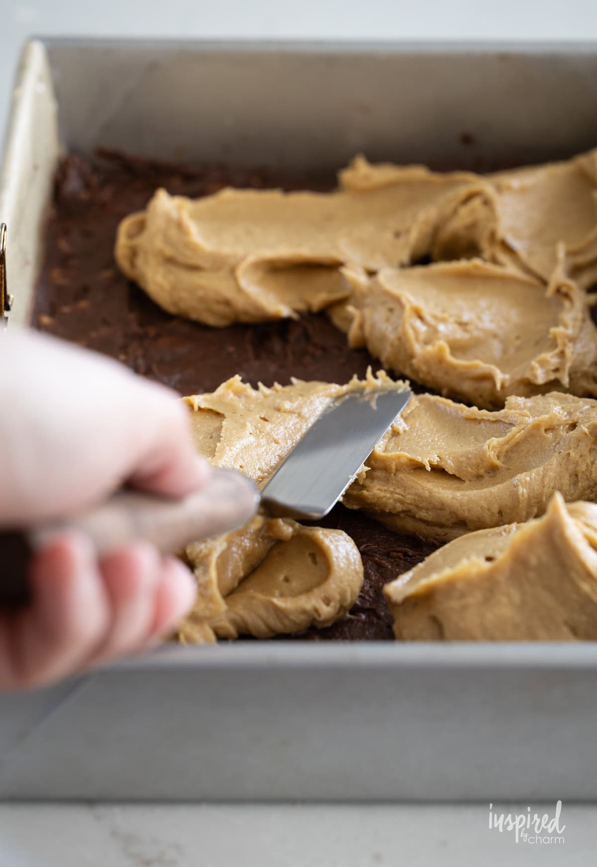 hand spreading peanut butter layer onto brownies.