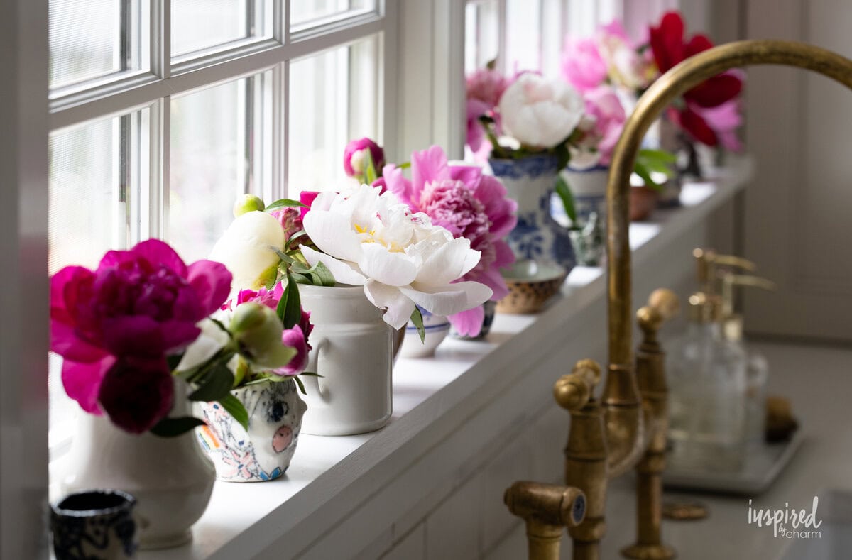 pitchers filled up with peonies lined up on a windowsill. 