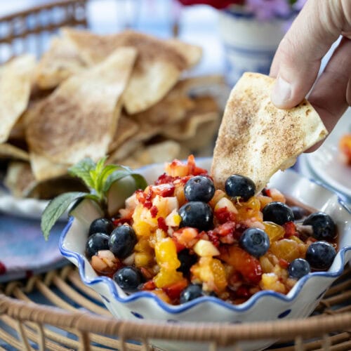 hand with tortilla chips dipping into fruit salsa.