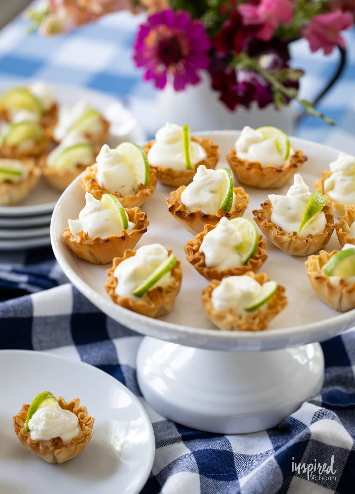 Key Lime Pie Tartlets on a cake stand and plate on a table. 