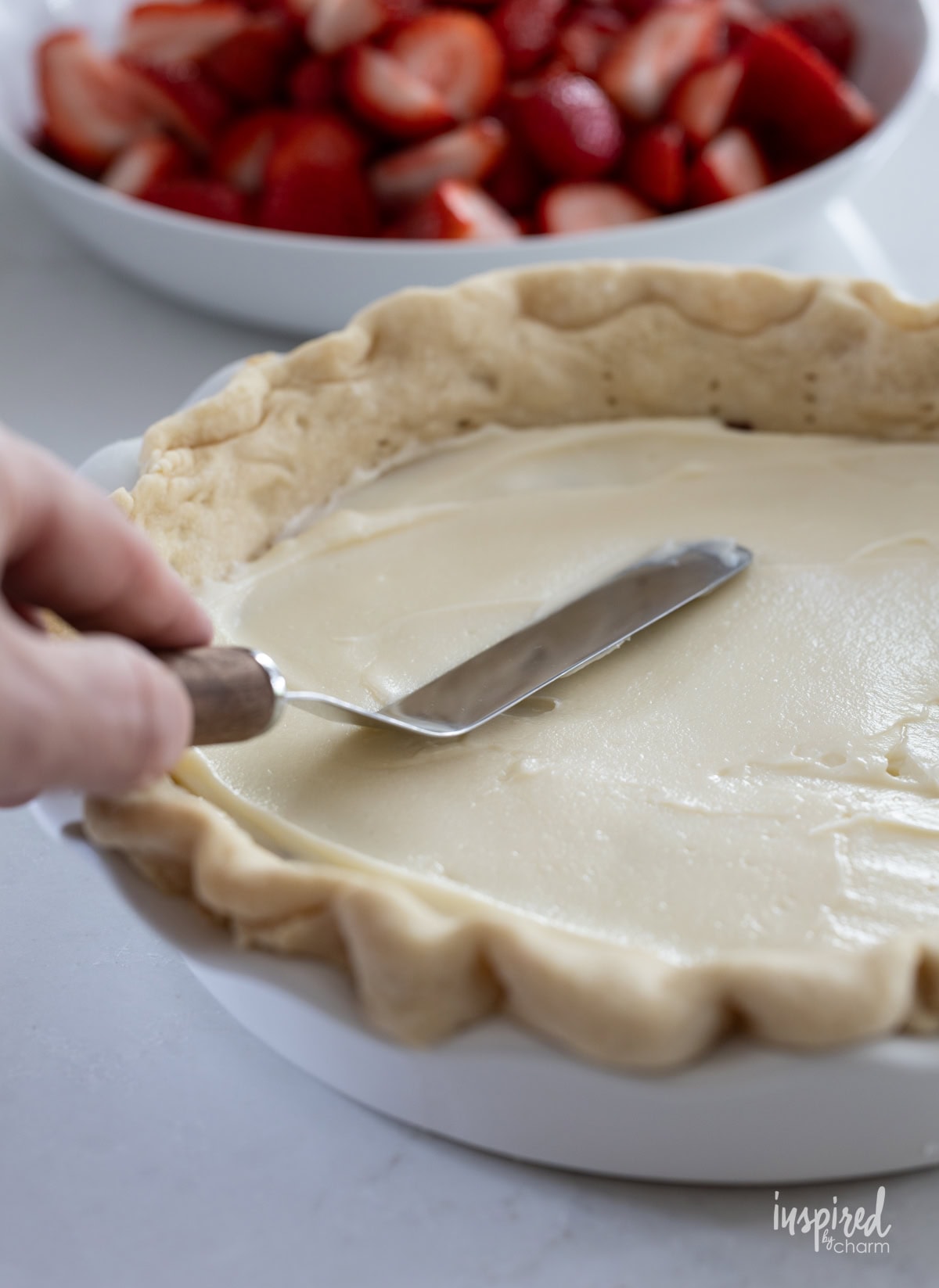 hand with spatula spreading cream cheese layer into pie crust.