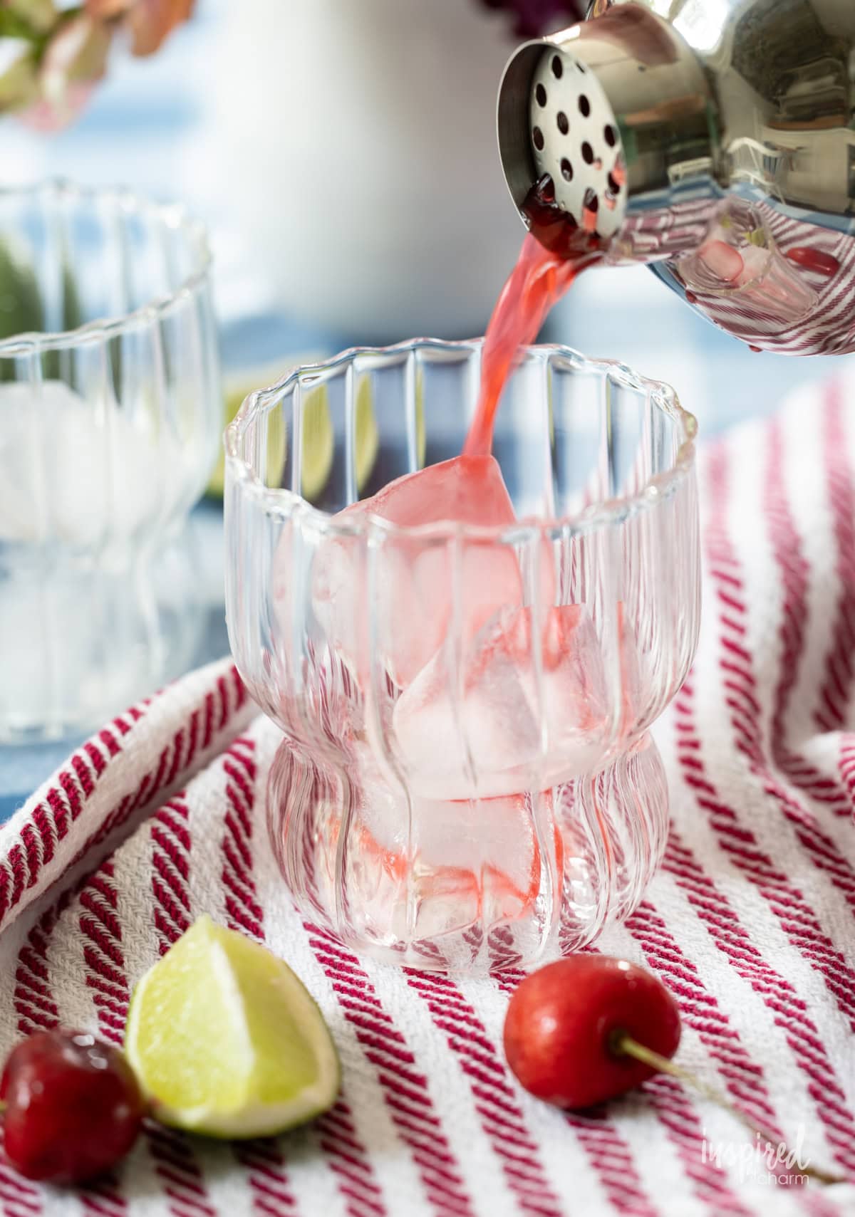 straining cherry lime splash cocktail into glass with ice.