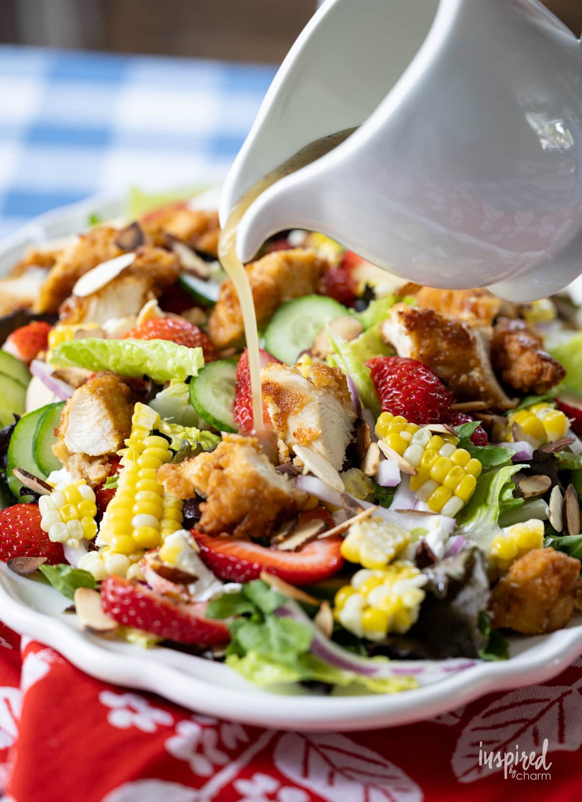 hand with pitcher pouring dressing onto Crispy Chicken Strawberry Corn Salad.