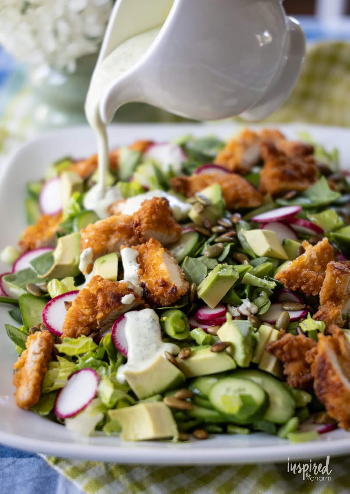 hand pouring dressing onto green goddess salad.