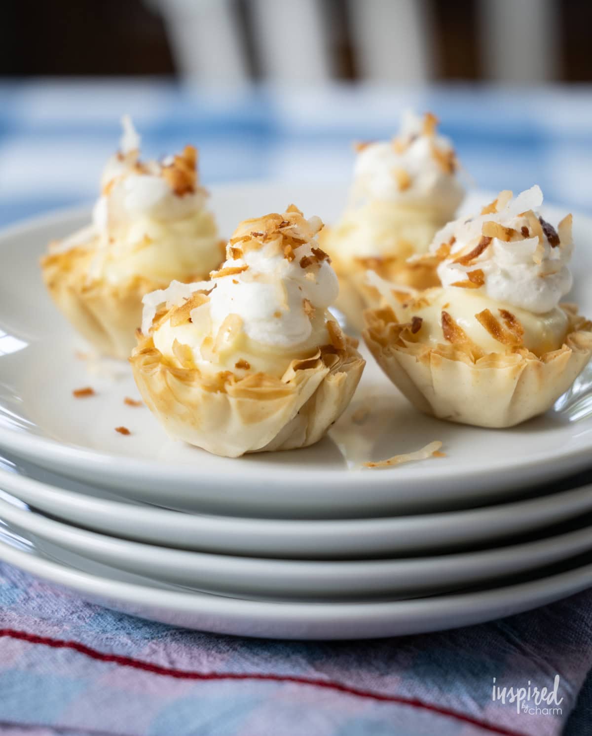 four Mini Coconut Cream Pie Tartlets  on a stack of plates.